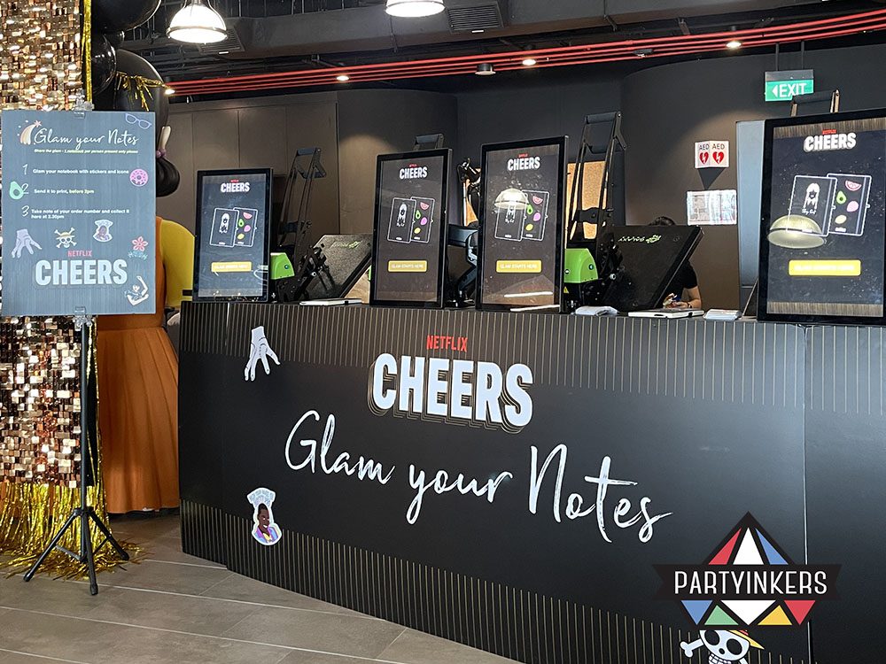 A stylish event booth branded "Netflix Cheers" with sleek screens and equipment for personalizing notebooks.