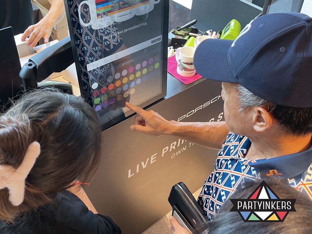 A close-up of event attendees interacting with the live printing station, selecting custom designs on a touchscreen interface.