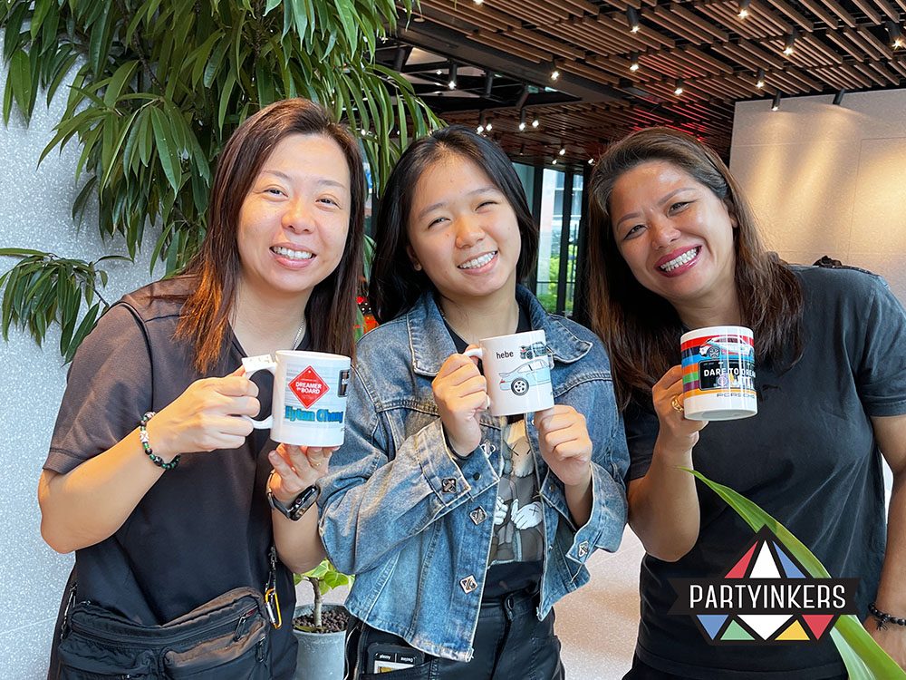 Three smiling event attendees holding their personalized Porsche mugs, celebrating the creative and interactive experience.