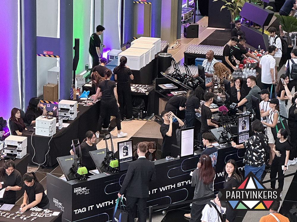 Partyinkers live printing booth at a corporate event, with attendees customizing products and staff assisting them.