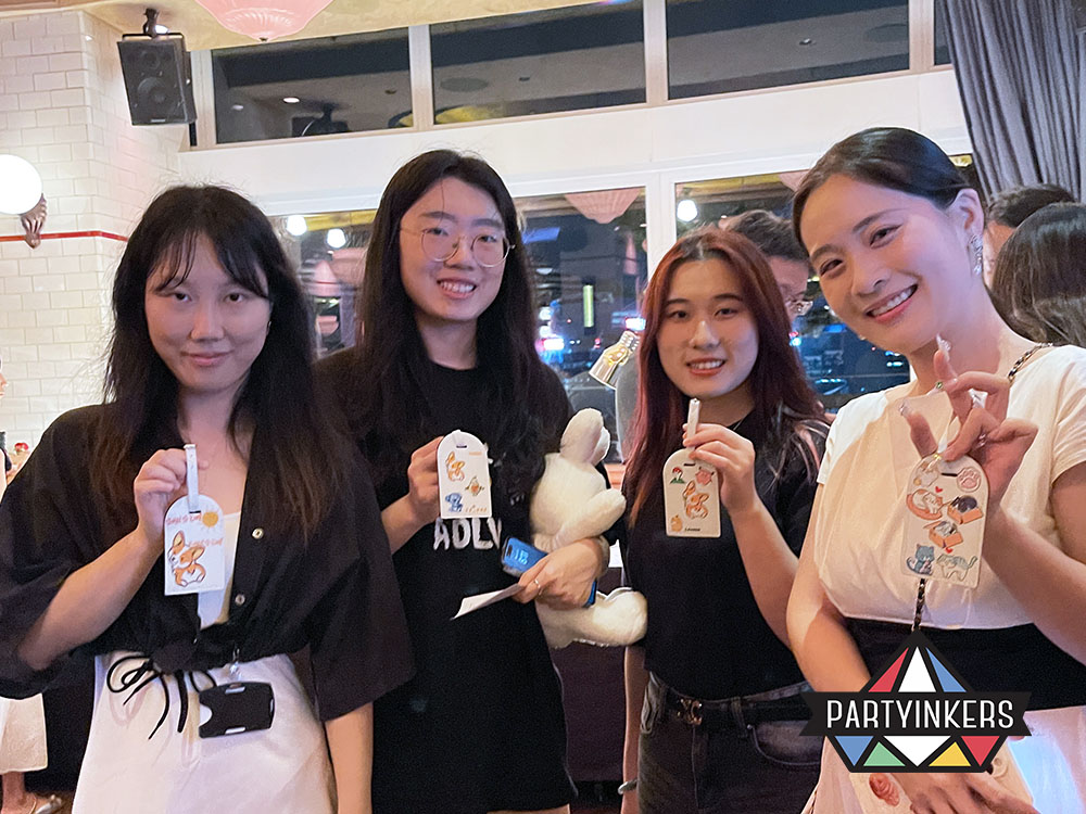 Four women proudly display their customized keychains at an interactive booth. Personalized giveaways like these are effective brand activation ideas for increasing audience engagement.