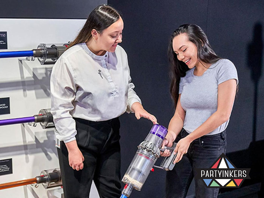 A Dyson brand activation idea demonstrating product performance to potential customers. A brand representative provides a hands-on experience with the latest vacuum technology, engaging shoppers in a direct and interactive way.