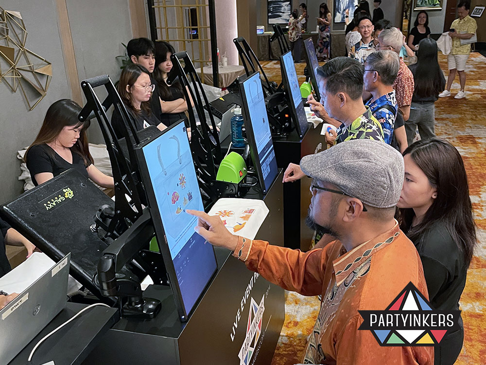 Attendees interact with touch-screen kiosks to customize tote bags at a live printing station during an event. This interactive setup is a great example of brand activation ideas that enhance customer participation.