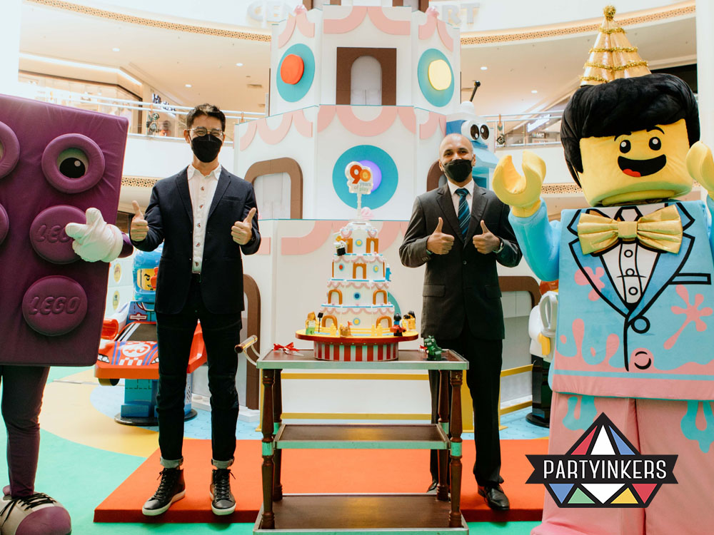 A LEGO-themed activation event featuring life-sized LEGO mascots, a colorful cake display, and corporate representatives, demonstrating a playful and engaging brand activation idea that captivates audiences.