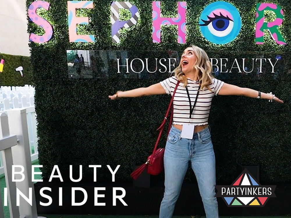  A cheerful woman posing in front of a vibrant Sephora Beauty Insider event backdrop, showcasing an engaging brand activation idea that enhances customer interaction through experiential marketing.