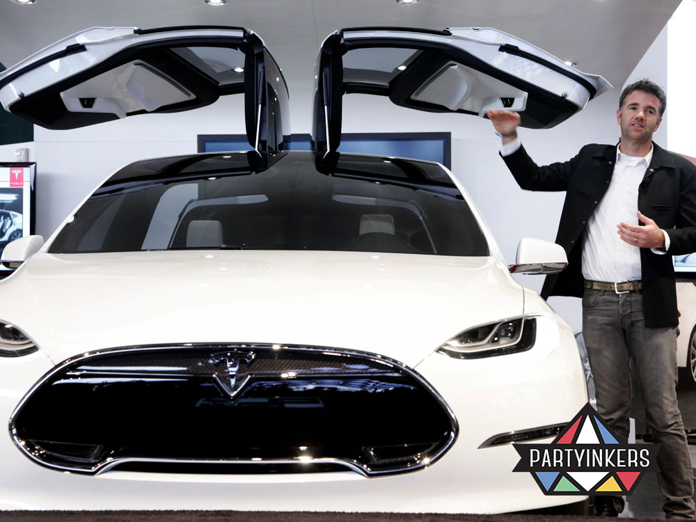 A Tesla representative presenting a futuristic car model with signature falcon-wing doors at a product launch event, exemplifying an innovative brand activation idea that highlights cutting-edge technology.