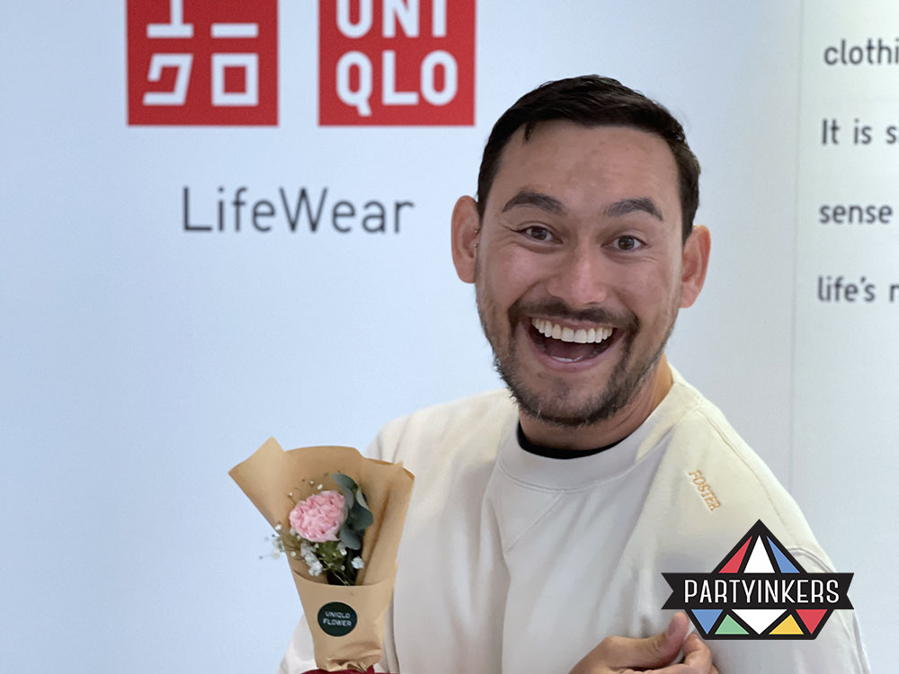 Celebrity Paul foster poses in front of a Uniqlo LifeWear display, holding a small bouquet of flowers. This brand activation idea showcases customer engagement through personalized experiences.